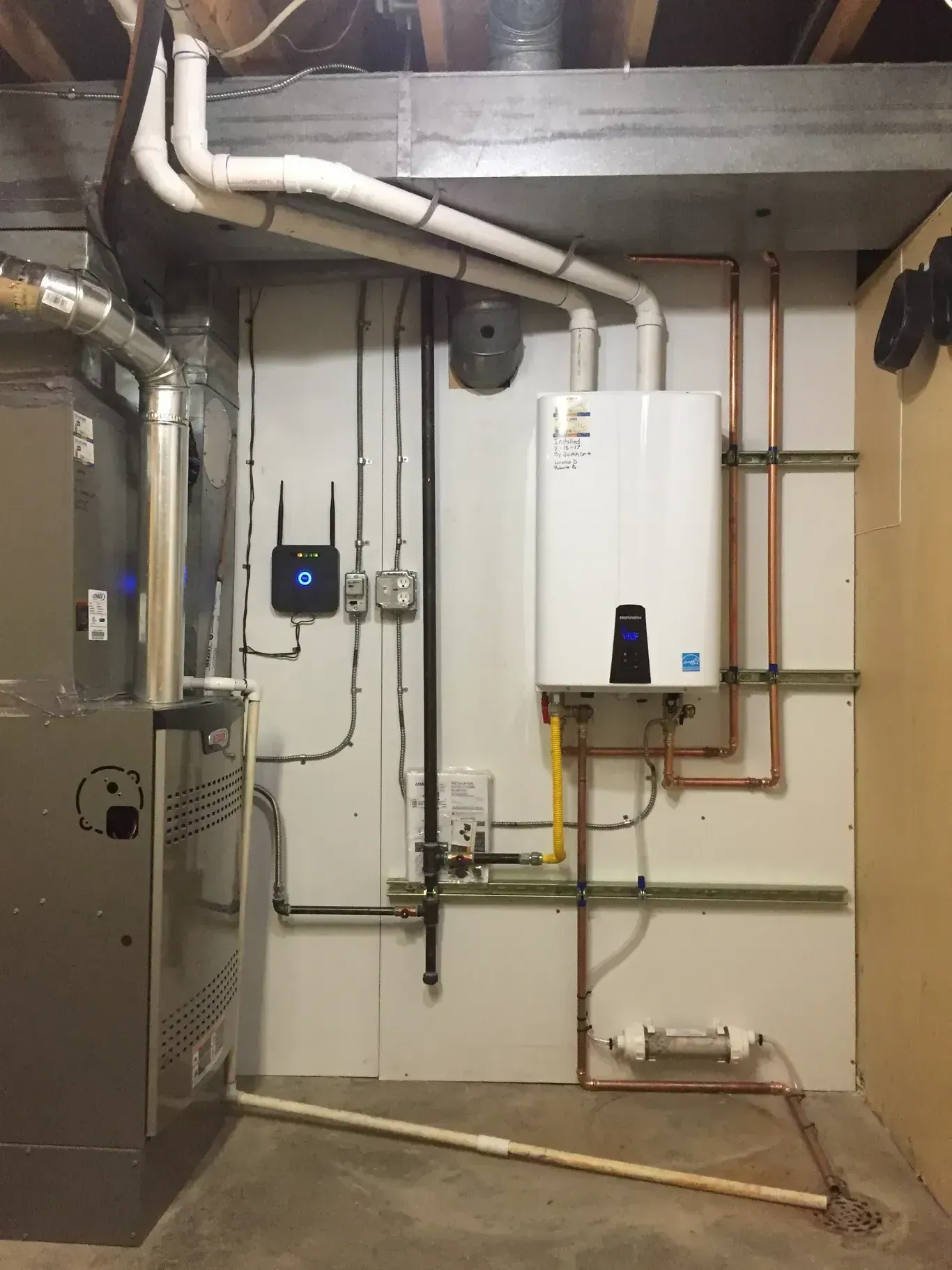 Water heater and furnace installed in a basement, with copper pipes and gas lines against a white wall.