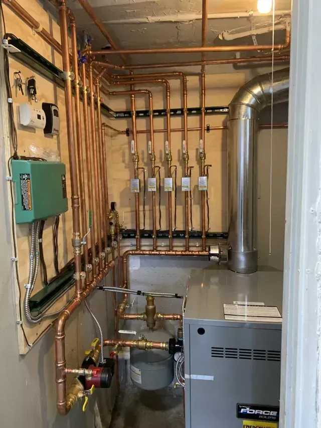 Copper pipes and a furnace in a utility room. Electrical box and valves are visible.