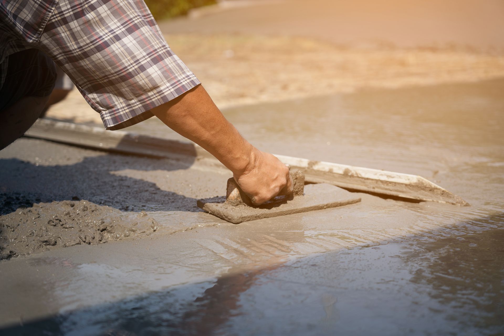 construction worker's gloved hands using trowel to scrape excess mix level with wood forms freshly poured concrete pad