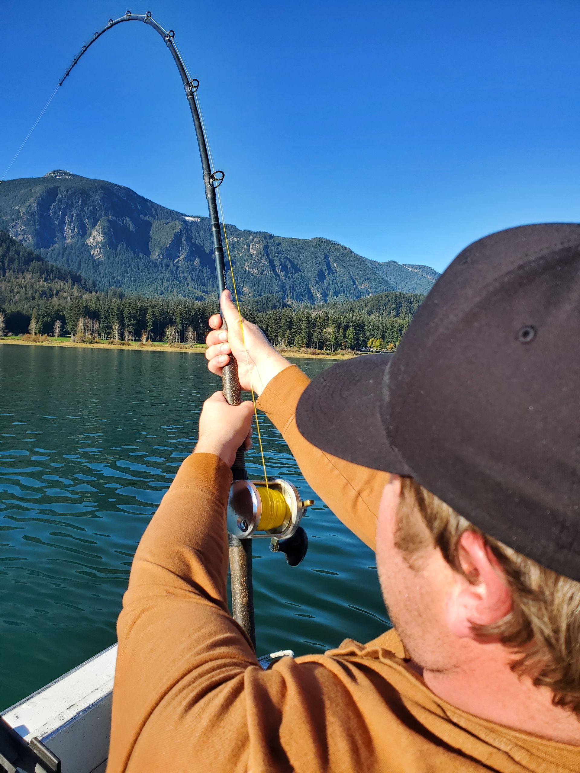 Person fishing on a lake with a bent rod, blue water, and mountains in the background