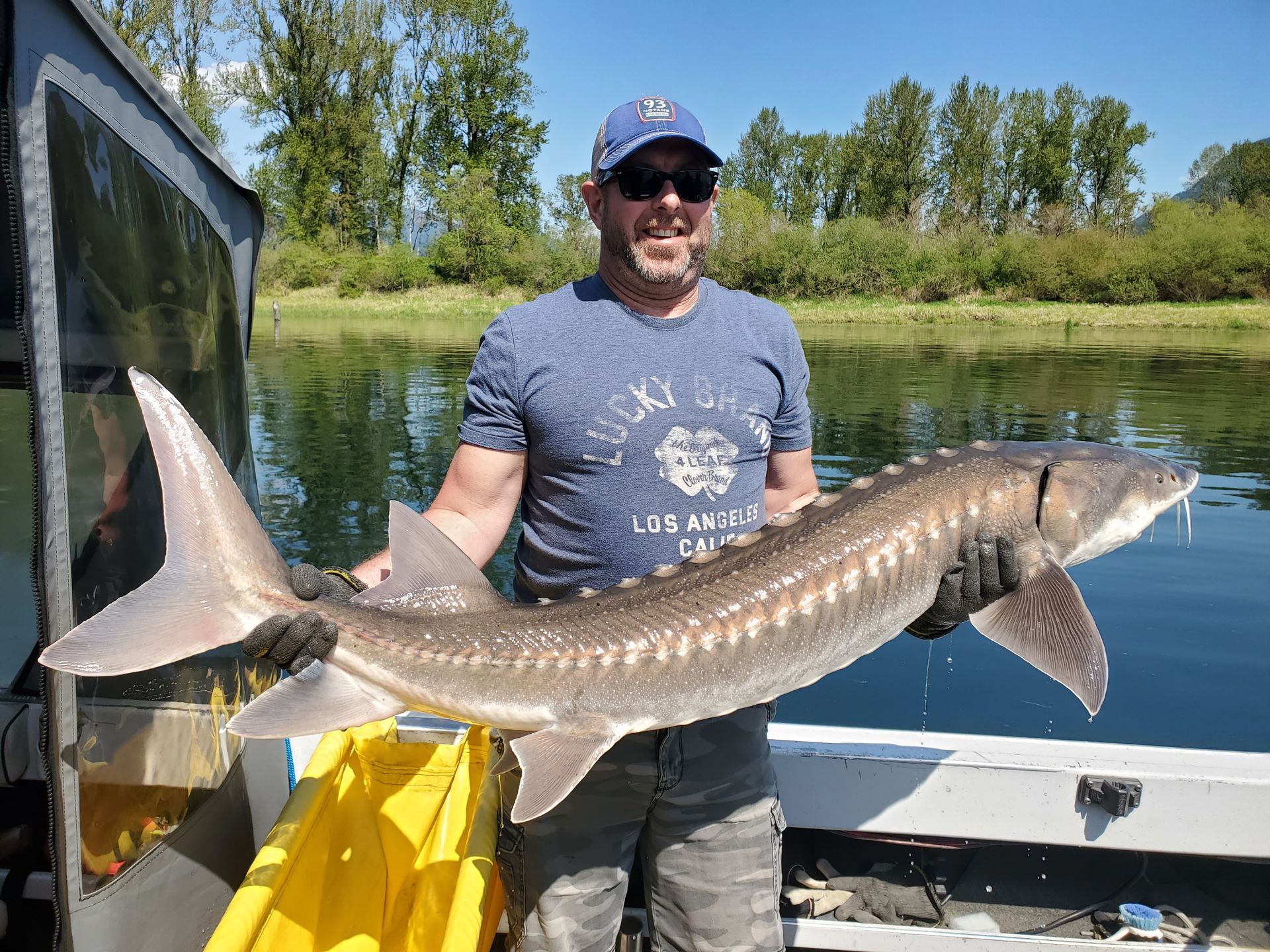 Man holding a large sturgeon on a boat by a calm river