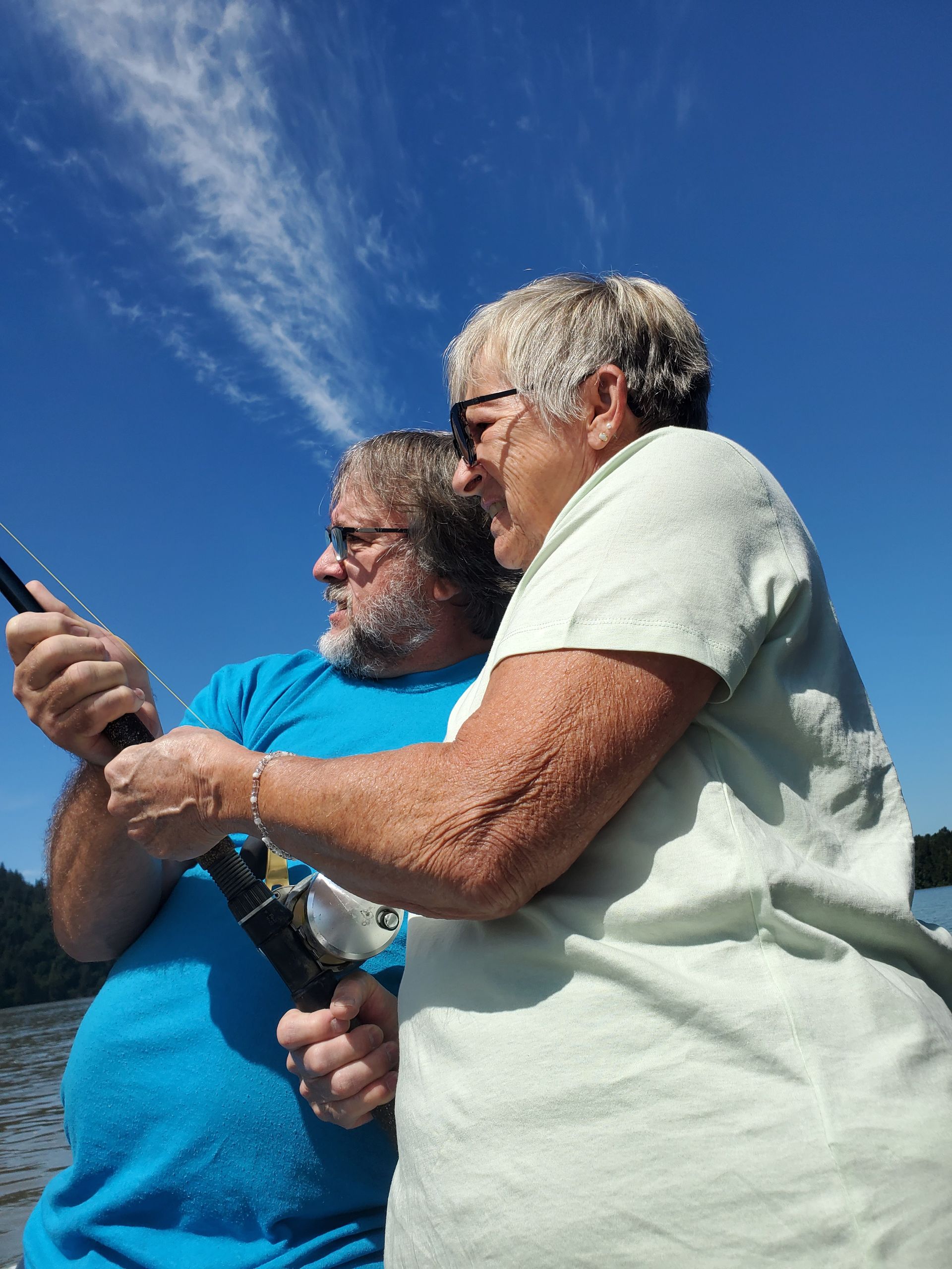 Two people outdoors under a blue sky, looking at a phone and holding a fishing rod.