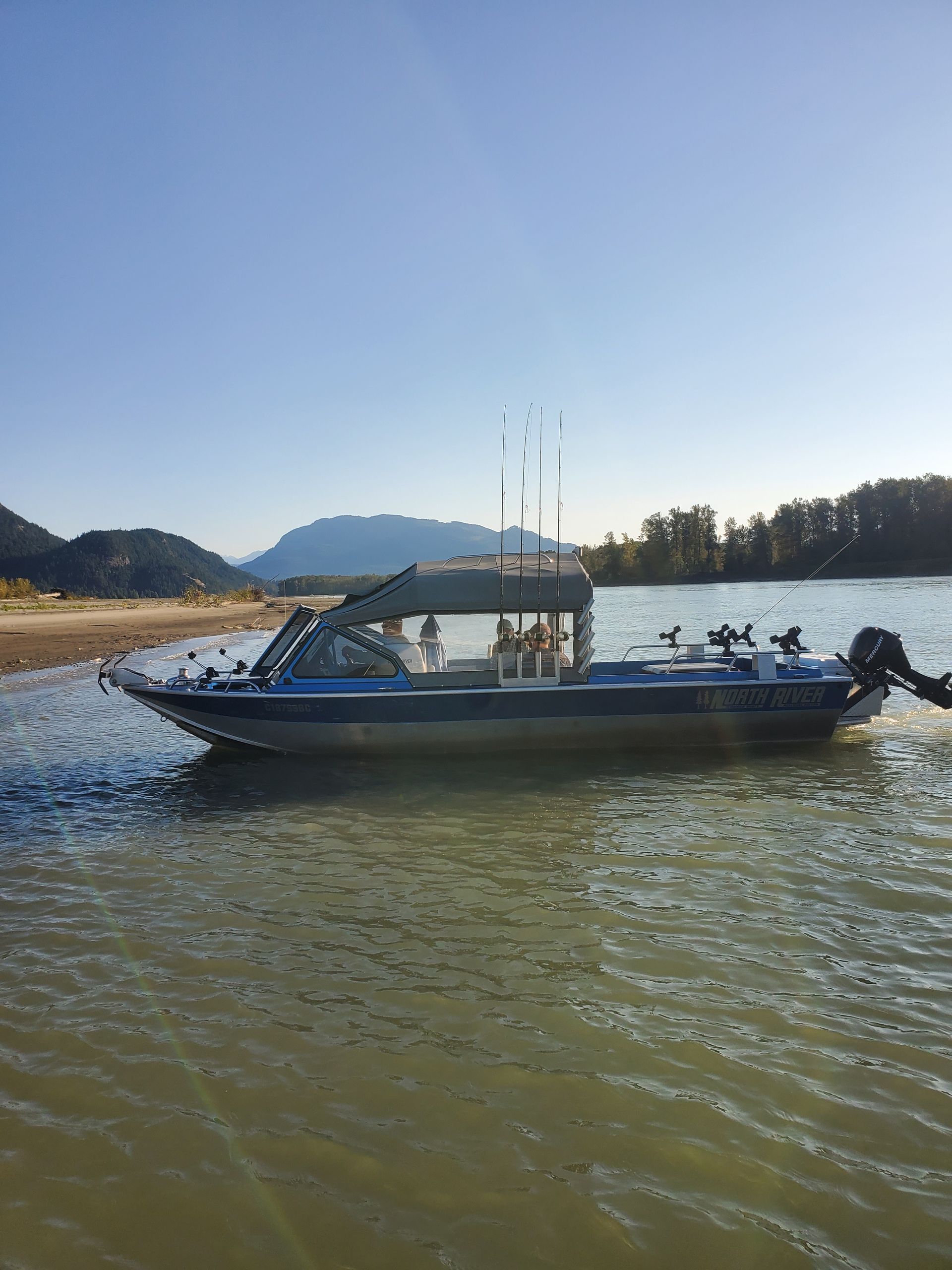 Blue boat on calm water near shore, with mountains and a clear sky in the background.