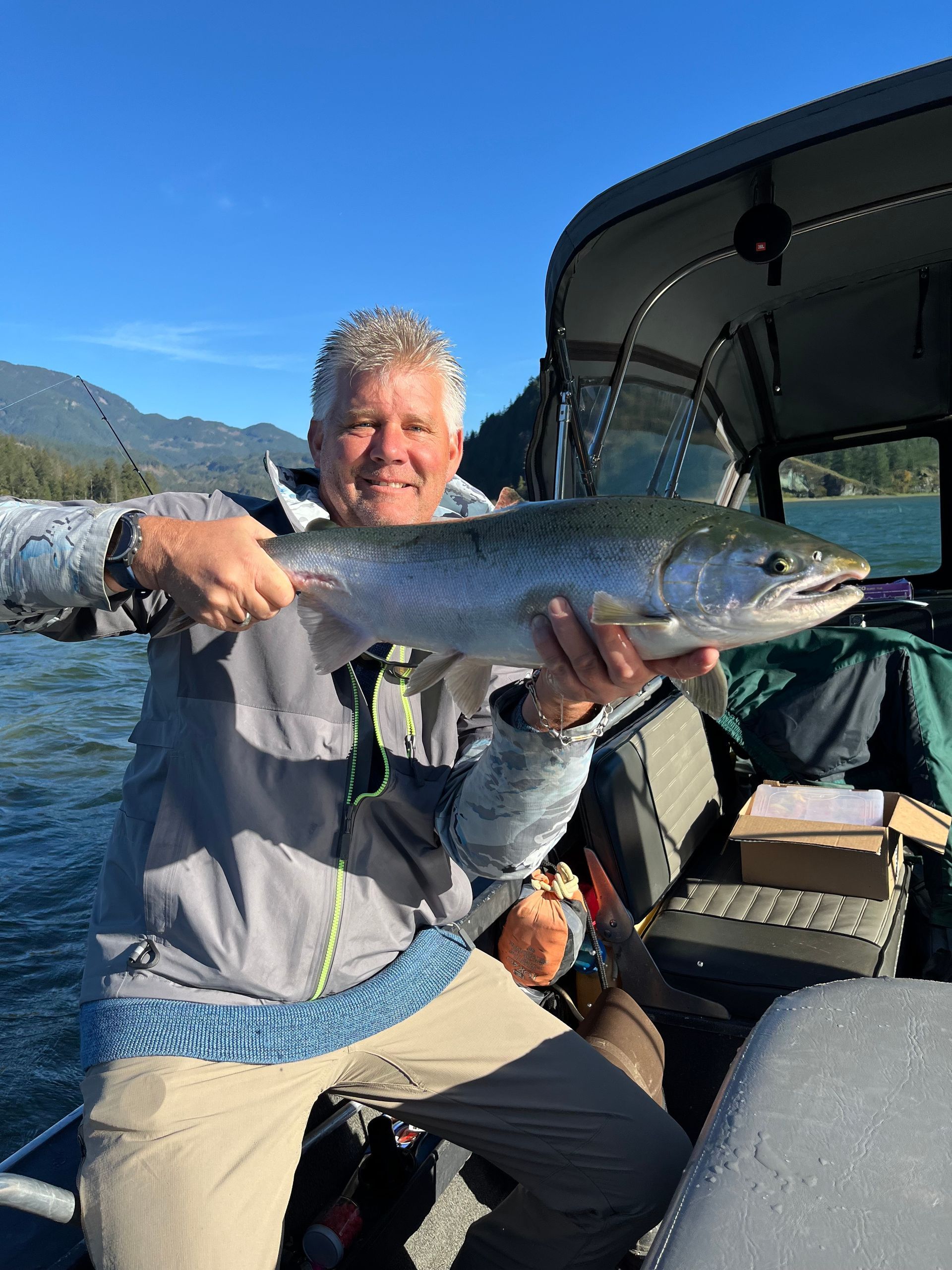Person holding a large fish on a boat with water and mountains in the background
