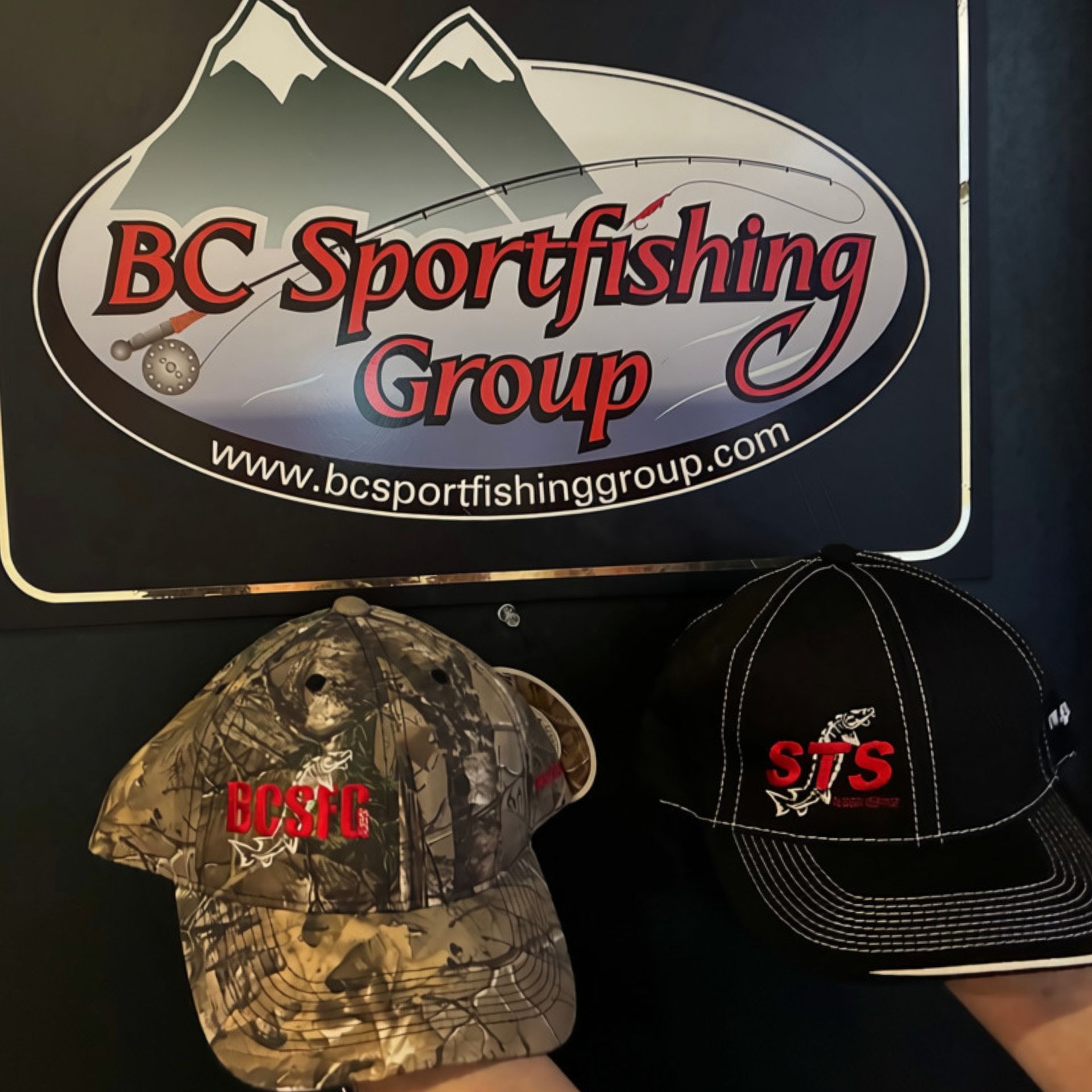 BC Sportfishing Group banner with two branded hats, one camouflage and one black, on a dark background