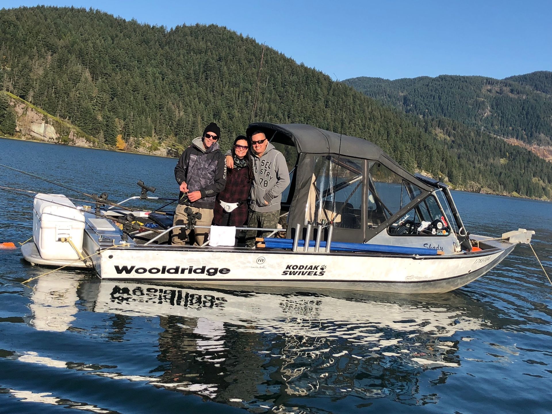 Four people on a small motorboat on a lake, with forested hills in the background.
