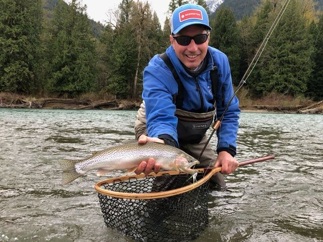 Angler in blue jacket holding a large fish in a net in a river.