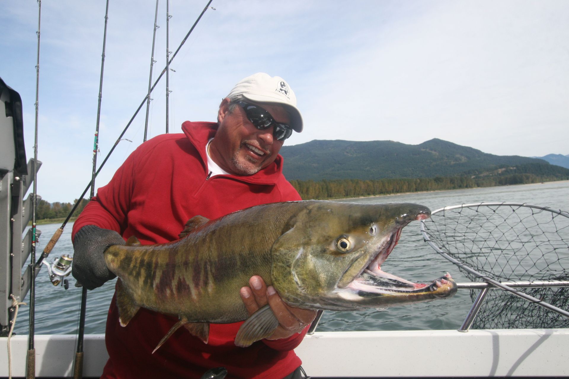 Smiling angler in red shirt holding a large fish on a boat by the water