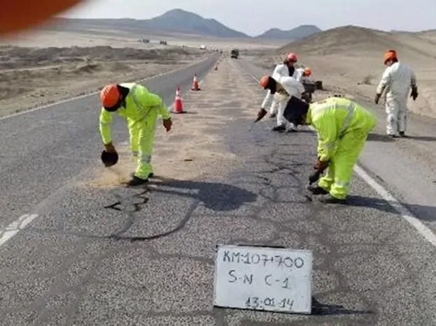 Obreros con trajes de seguridad fluorescentes reparan el asfalto agrietado en una carretera del desierto.