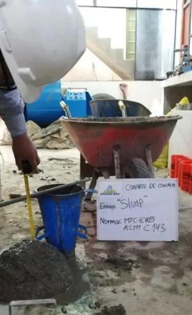 Un trabajador vierte material oscuro desde un gran embudo rojo en un recipiente azul en un taller interior.