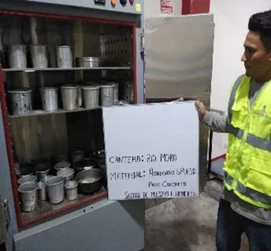 Un trabajador con chaleco amarillo abre un armario lleno de contenedores metálicos en una nave industrial.