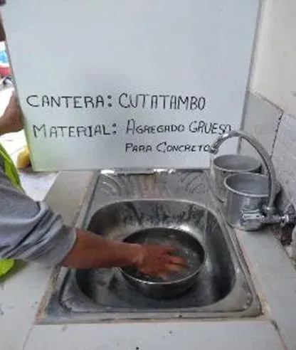 Una persona se lava las manos en un lavabo junto a un cartel en español que indica que hay un moho en una pila de hormigón.