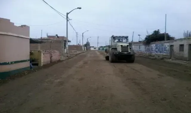 Camino de tierra en un barrio tranquilo con un camión grande que se dirige hacia la cámara bajo un cielo nublado.