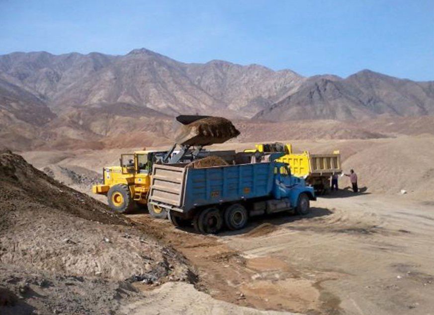 Un camión volquete amarillo está siendo cargado con tierra por una excavadora en una cantera rocosa del desierto.