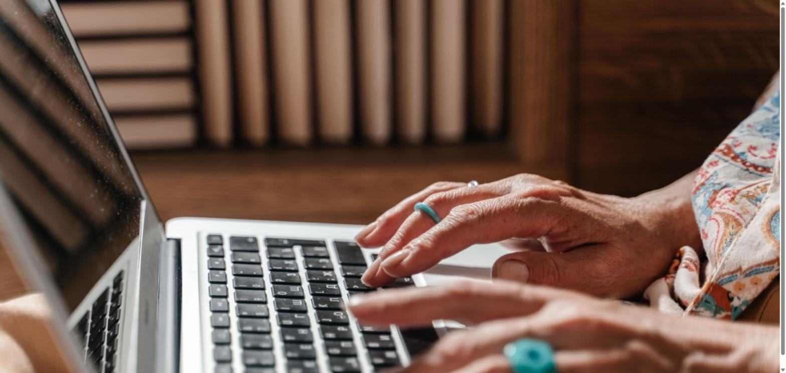 Older adult's hands wearing teal rings typing on a laptop keyboard