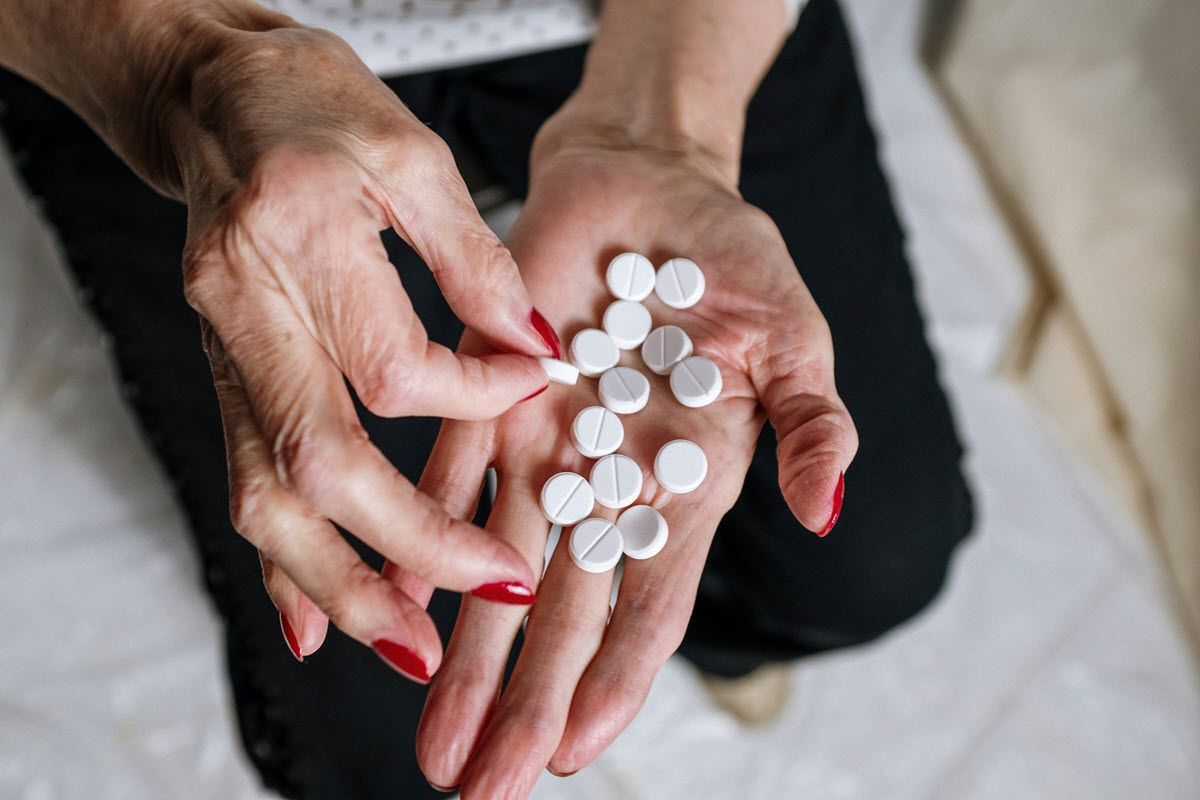 A pair of hands holding several small, round white pills against a background of dark trousers.