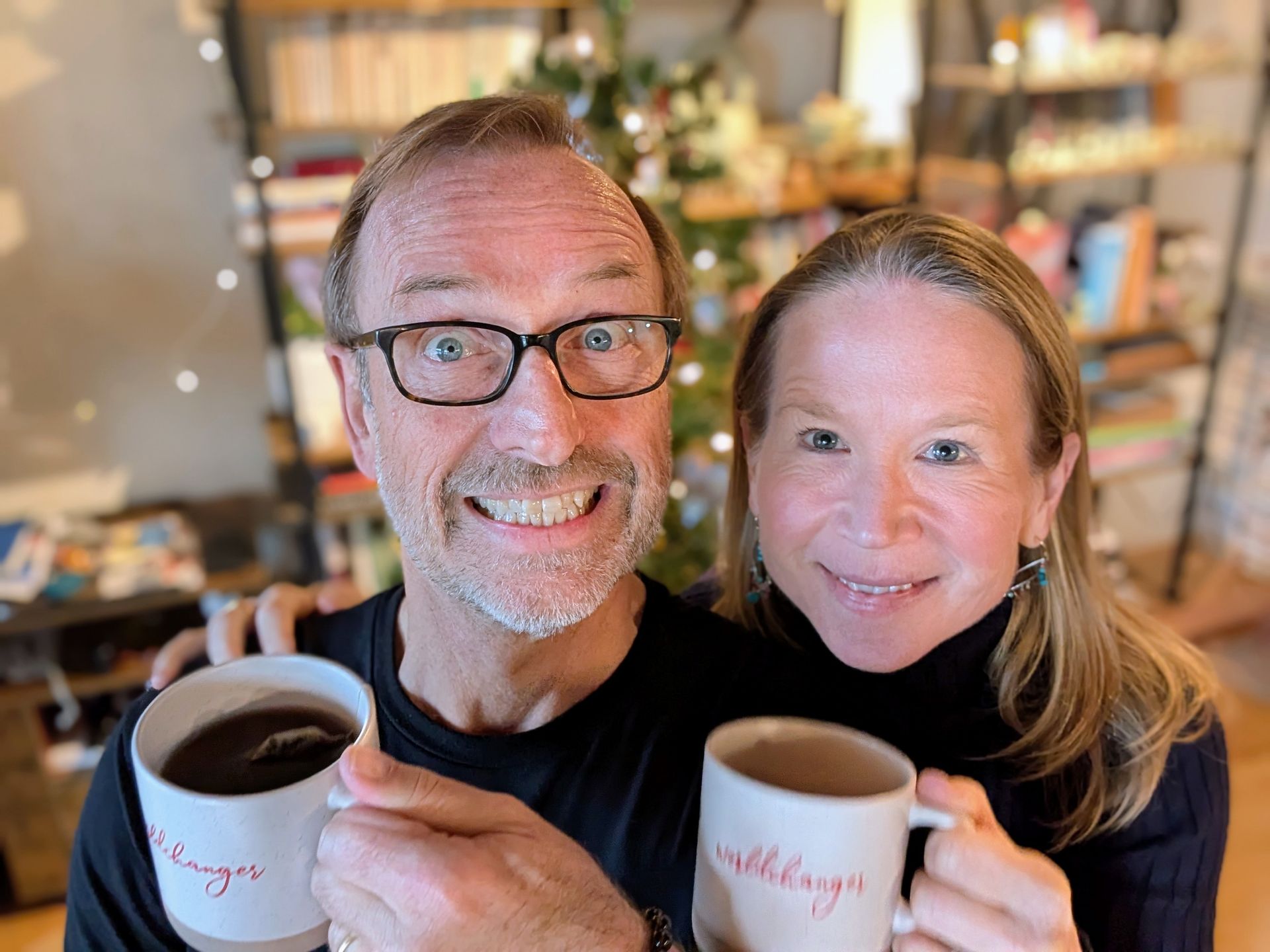 Jerry Michalski and April Rinne are holding coffee mugs in front of a christmas tree.