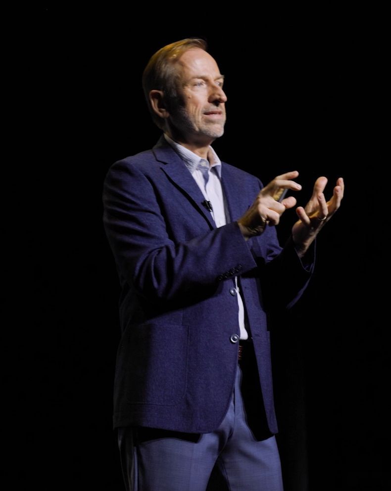 Jerry Michalski in a suit is standing on a stage with his hands in the air.