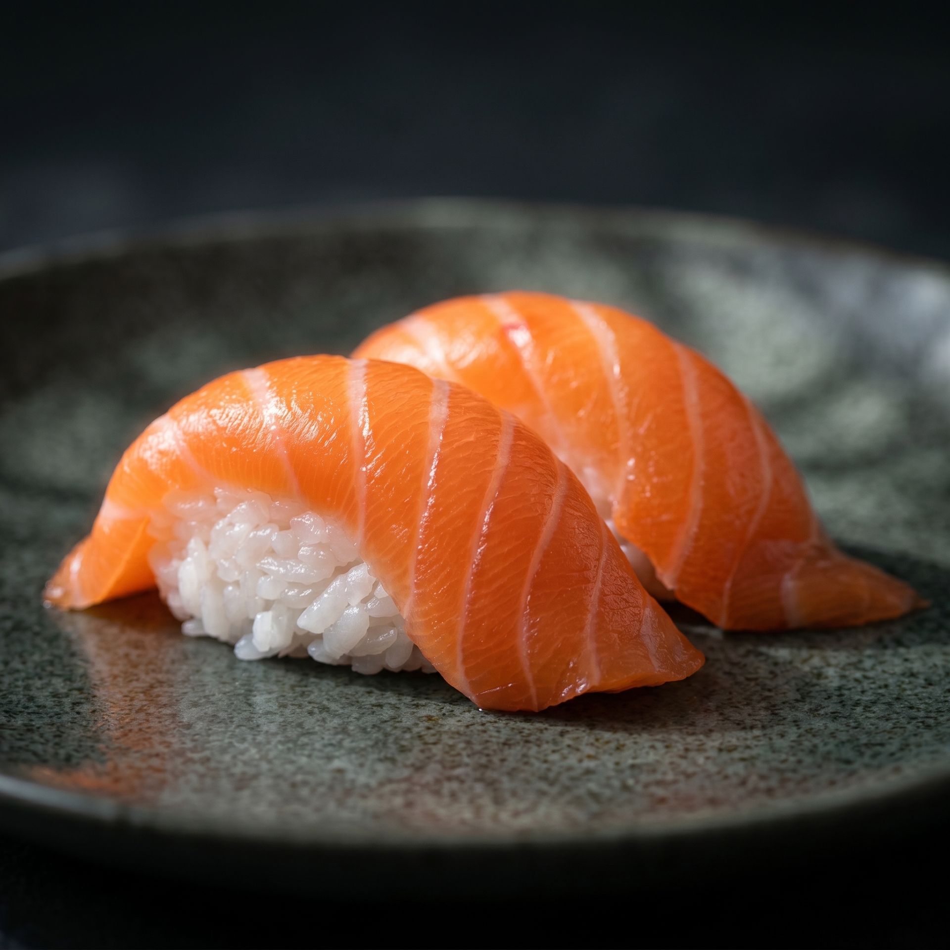 Salmon nigiri on a dark plate, with bright orange fish over white rice