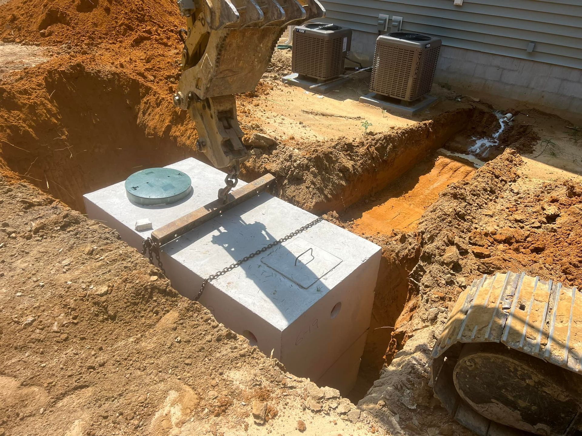 Professional excavation equipment preparing a property for moving and installing a heavy septic tank.