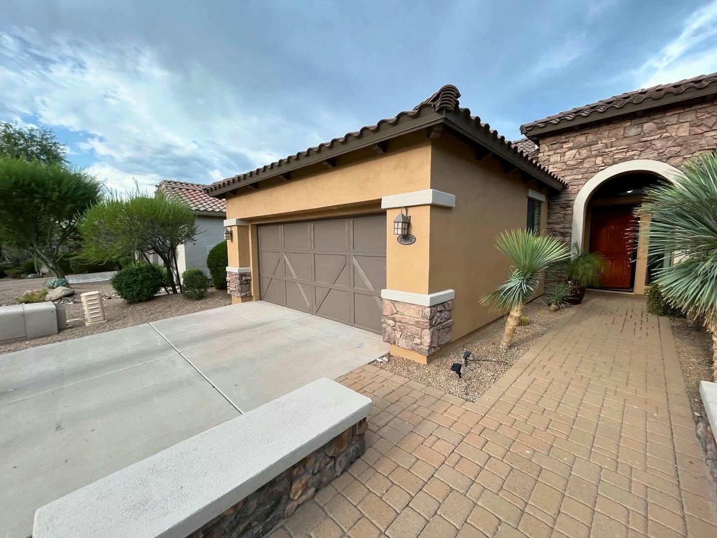 Tan stucco house with a beige garage door, brick pathway leading to a red door. Overcast sky.