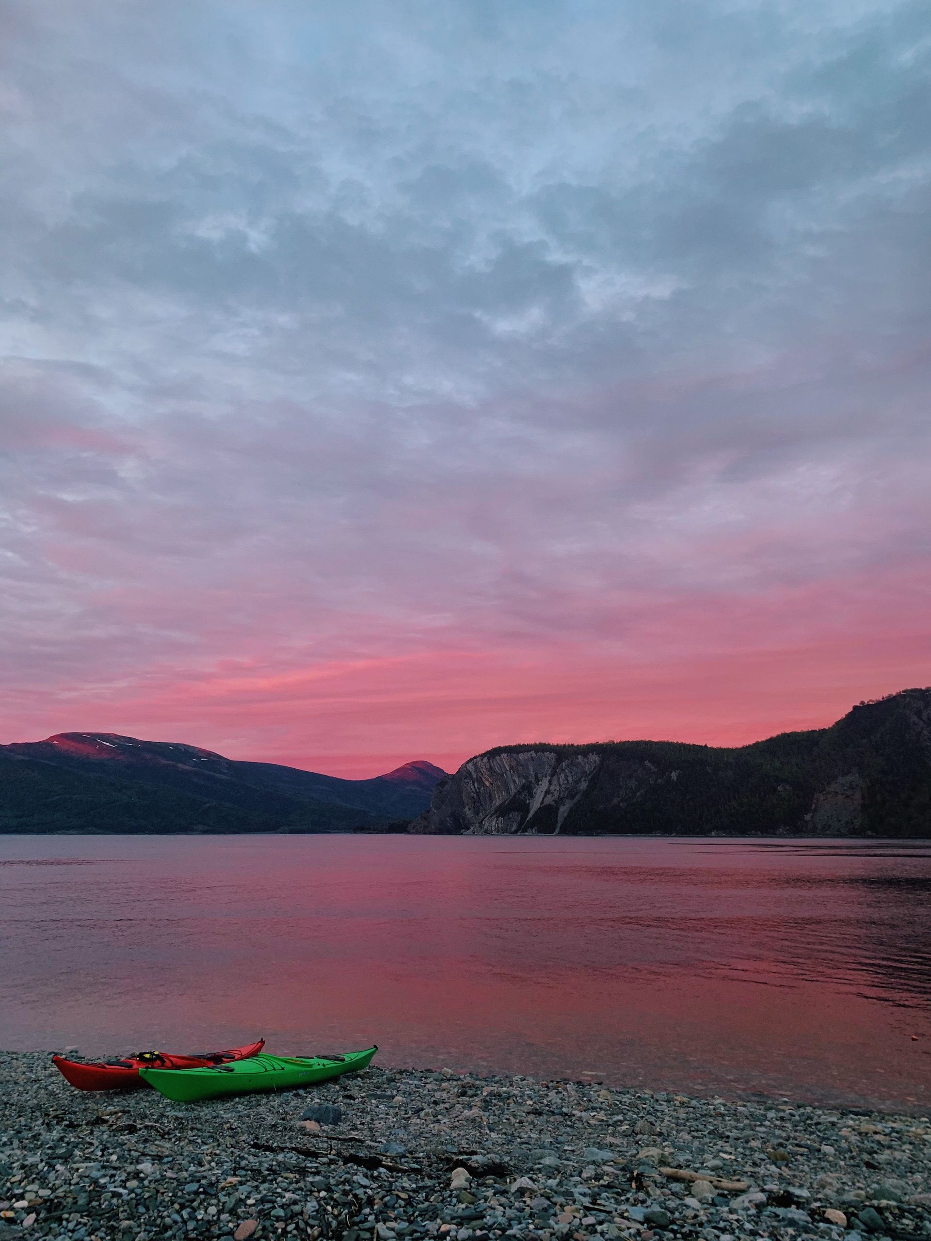 Two kayaks are sitting on the shore of a lake at sunset.