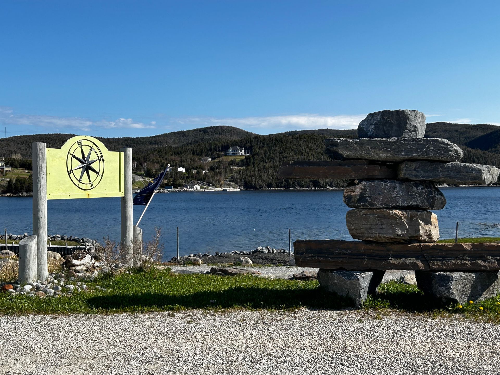 A stack of rocks sits in front of a lake with a sign in the background