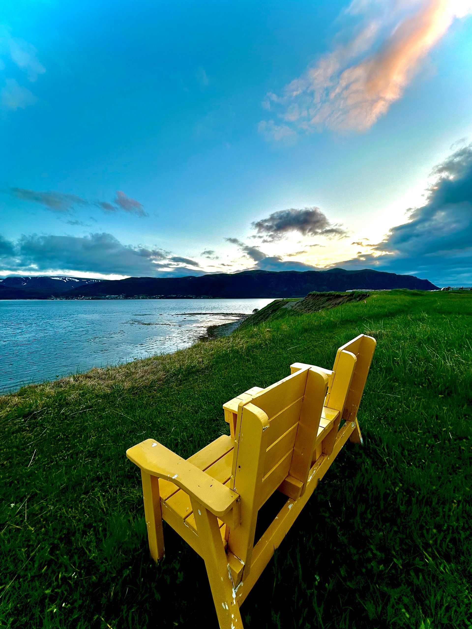 A yellow wooden bench is sitting in the grass near a body of water.