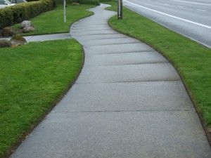 Curved concrete lawn edging along a well-maintained green yard beside a paved sidewalk and road
