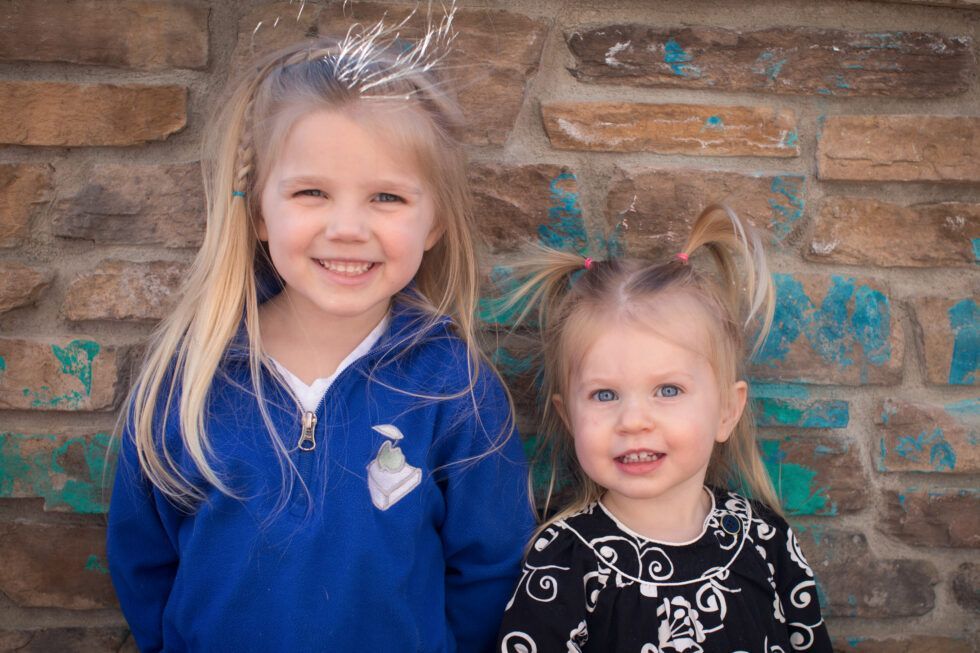Montessori children are standing next to each other in front of a brick wall