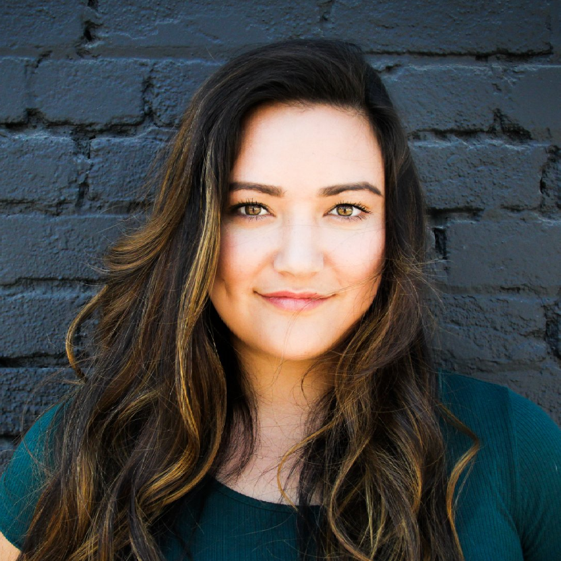 A woman with long hair is standing in front of a black brick wall.