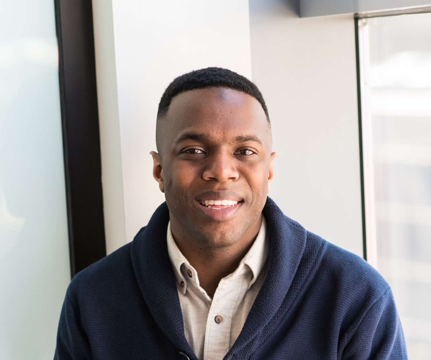 A man wearing a blue sweater and a white shirt is smiling for the camera.