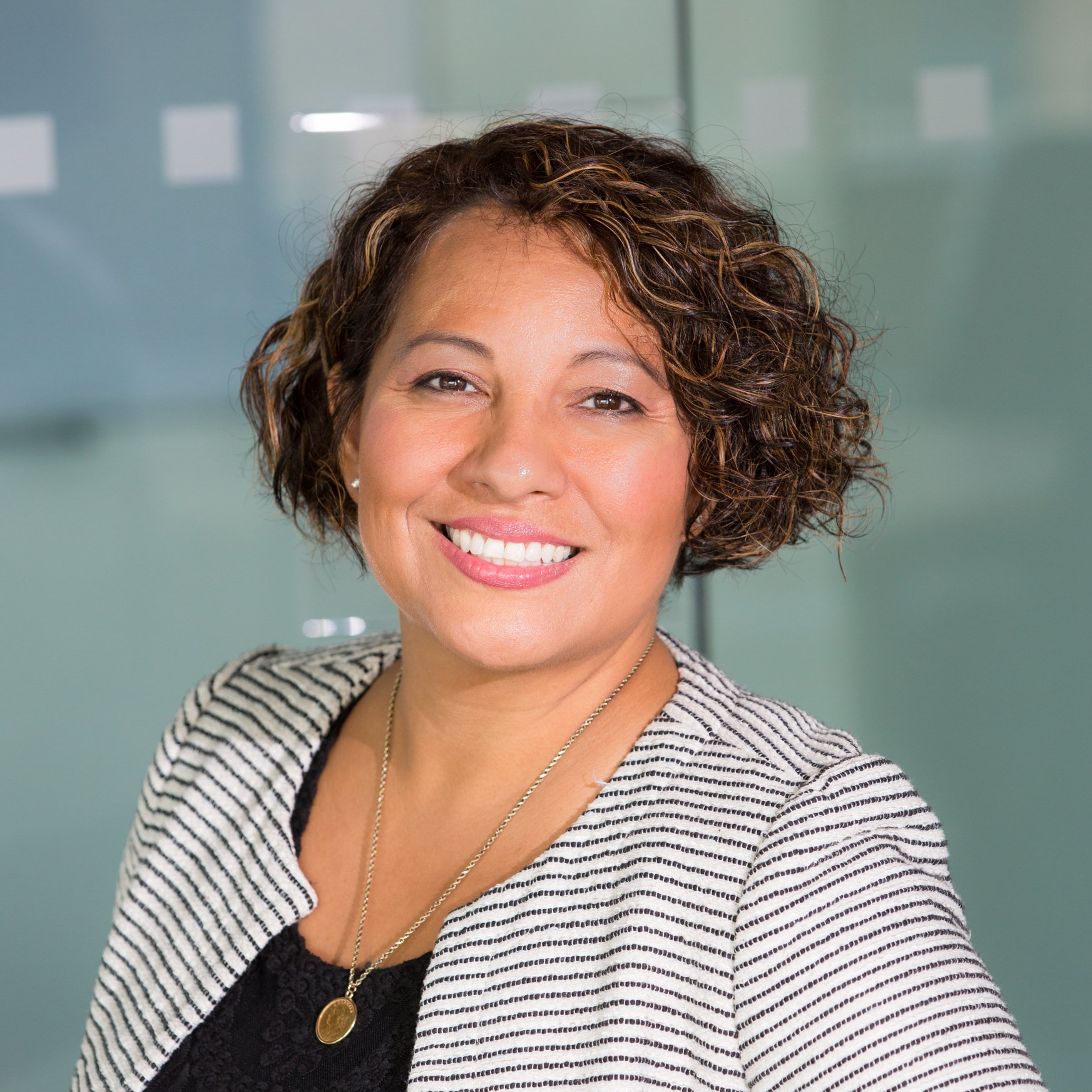 A woman wearing a striped jacket and a necklace is smiling for the camera.