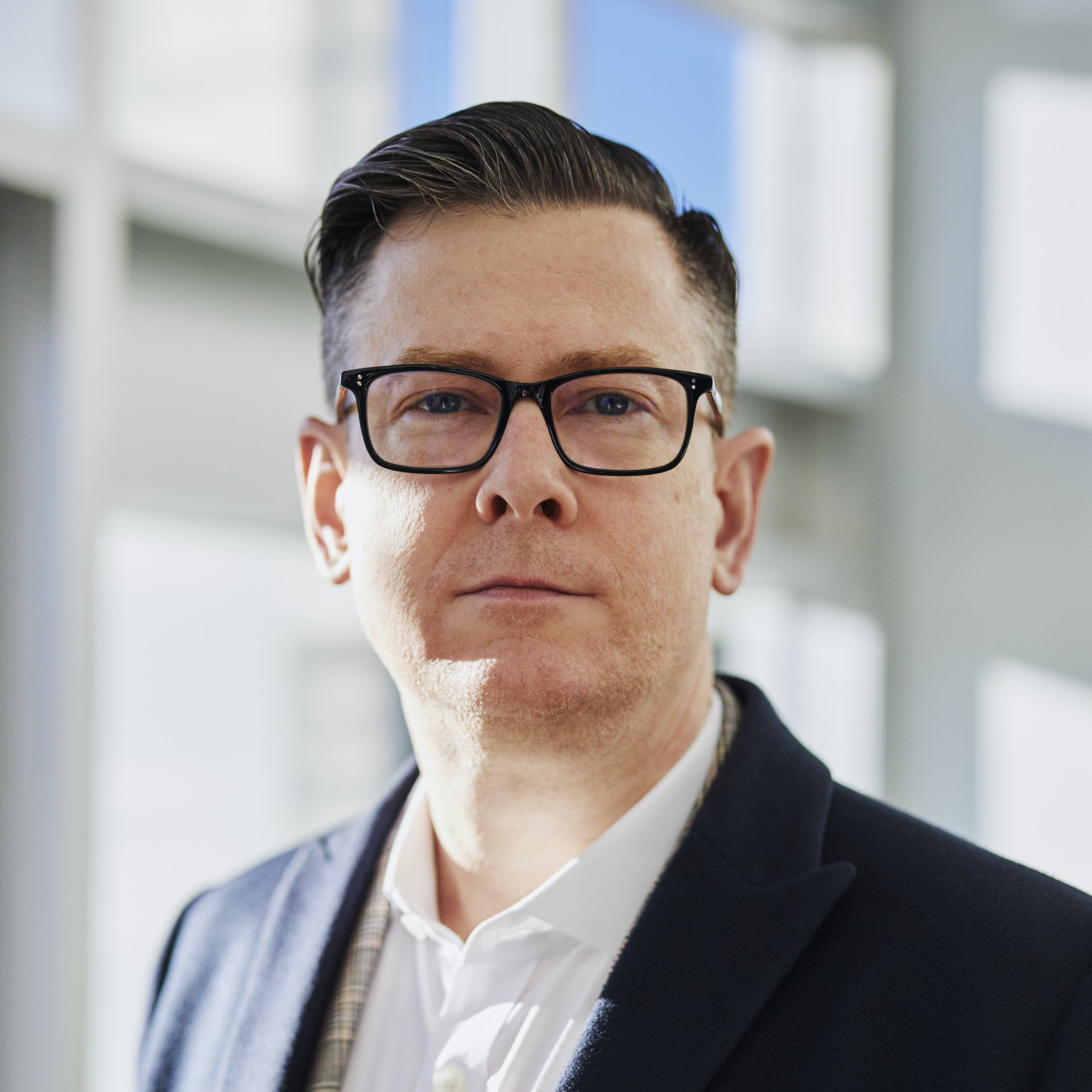 A man wearing glasses and a suit is looking at the camera.