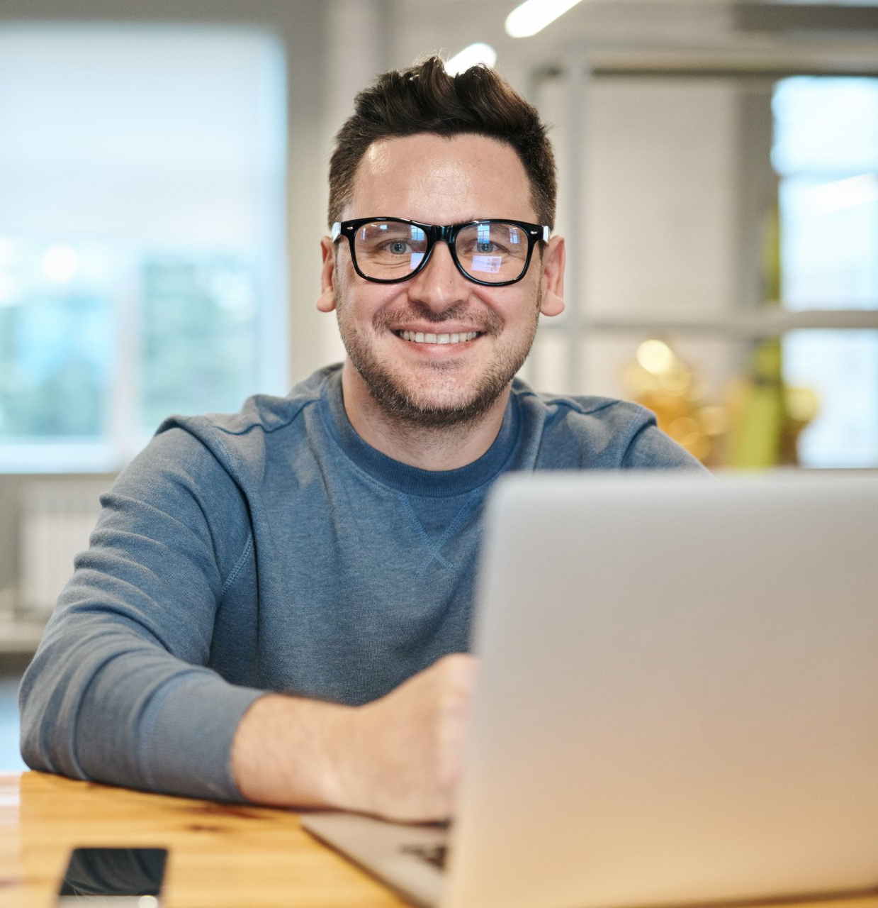 A man wearing glasses is sitting in front of a laptop computer.