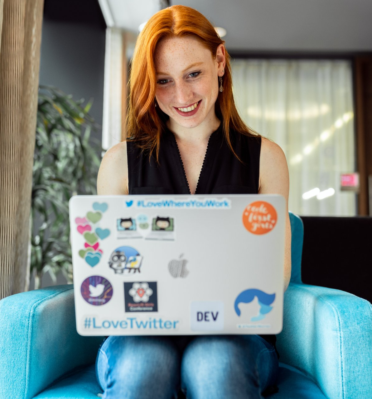A woman is sitting in a chair holding a laptop that says #lovetwitter