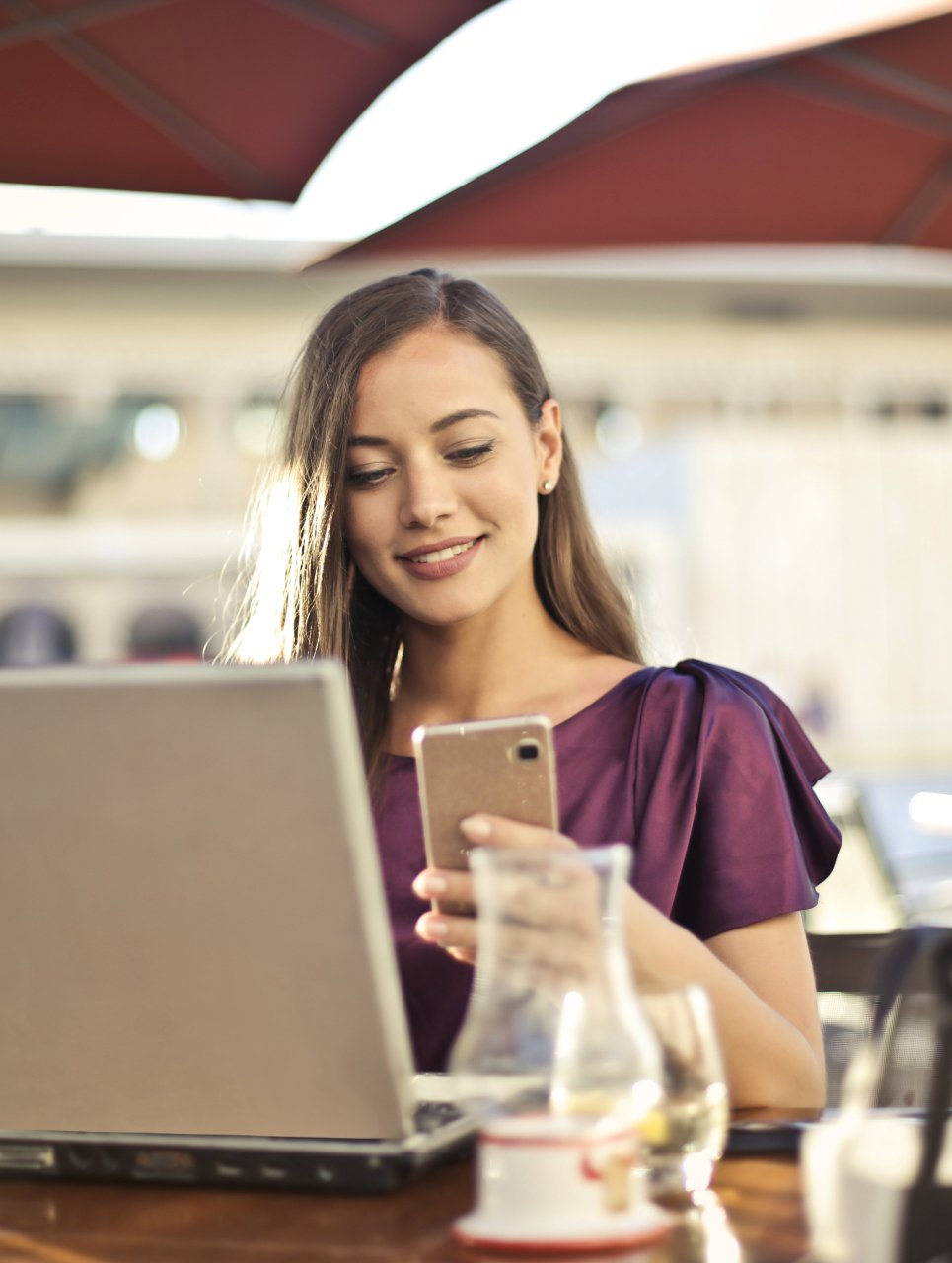 A woman is sitting at a table with a laptop and a cell phone.