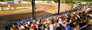 A large crowd of people are watching a race on a dirt track.
