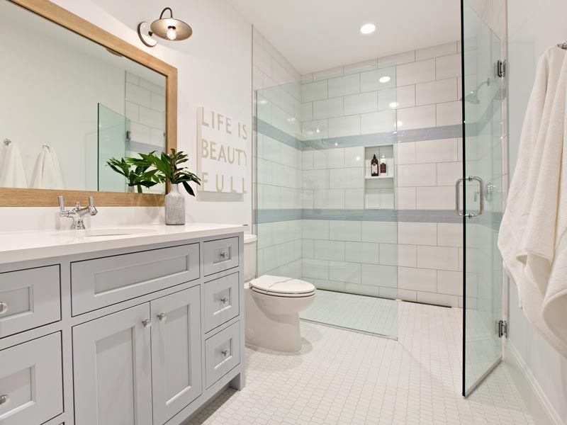 Bright modern white bathroom with double vanity, glass shower, and toilet