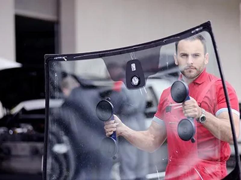 Man in a red shirt working on a car windshield with suction tools in a workshop