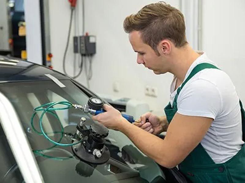 Technician using a tool to inspect a car windshield in an auto repair shop