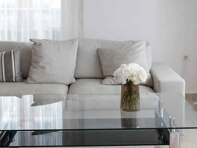 Minimalist living room with a light gray sofa and a glass coffee table holding white flowers.