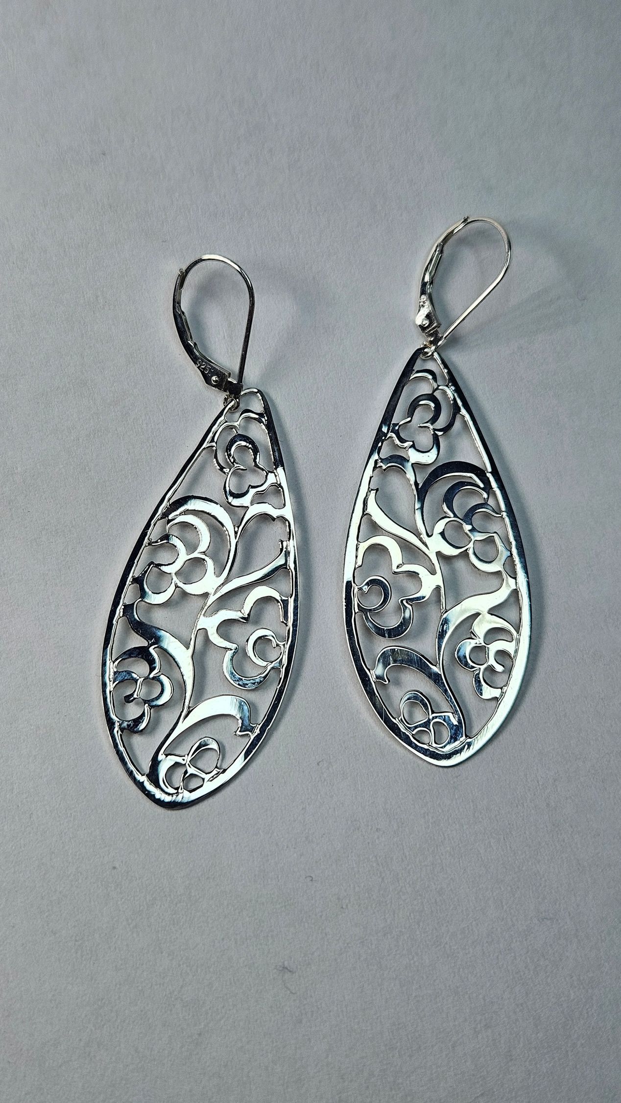 Pair of silver teardrop filigree earrings on a gray background