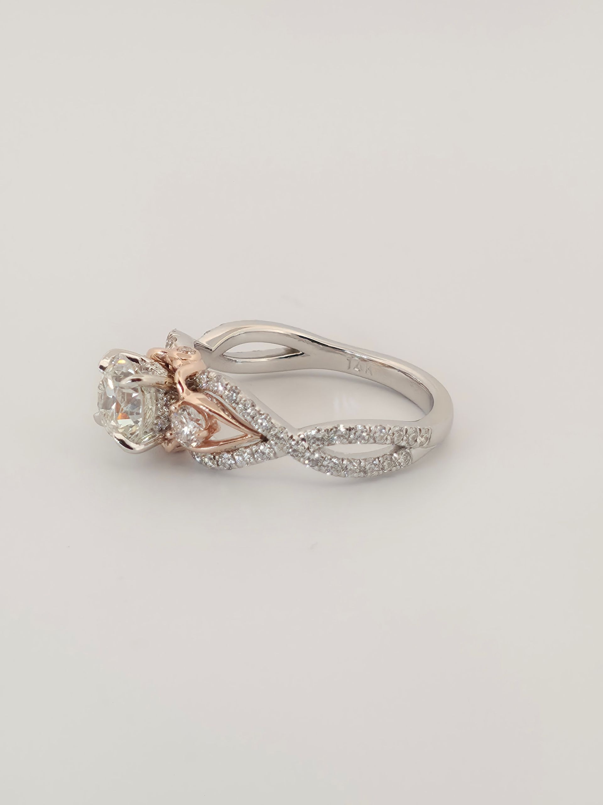 Silver and rose gold diamond ring with a clear center stone on a light background