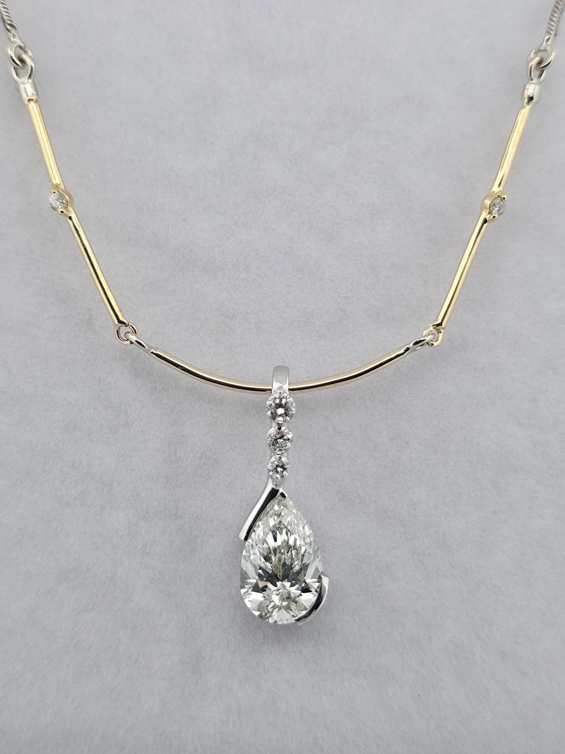 Gold necklace with a pear-shaped diamond pendant on a gray background