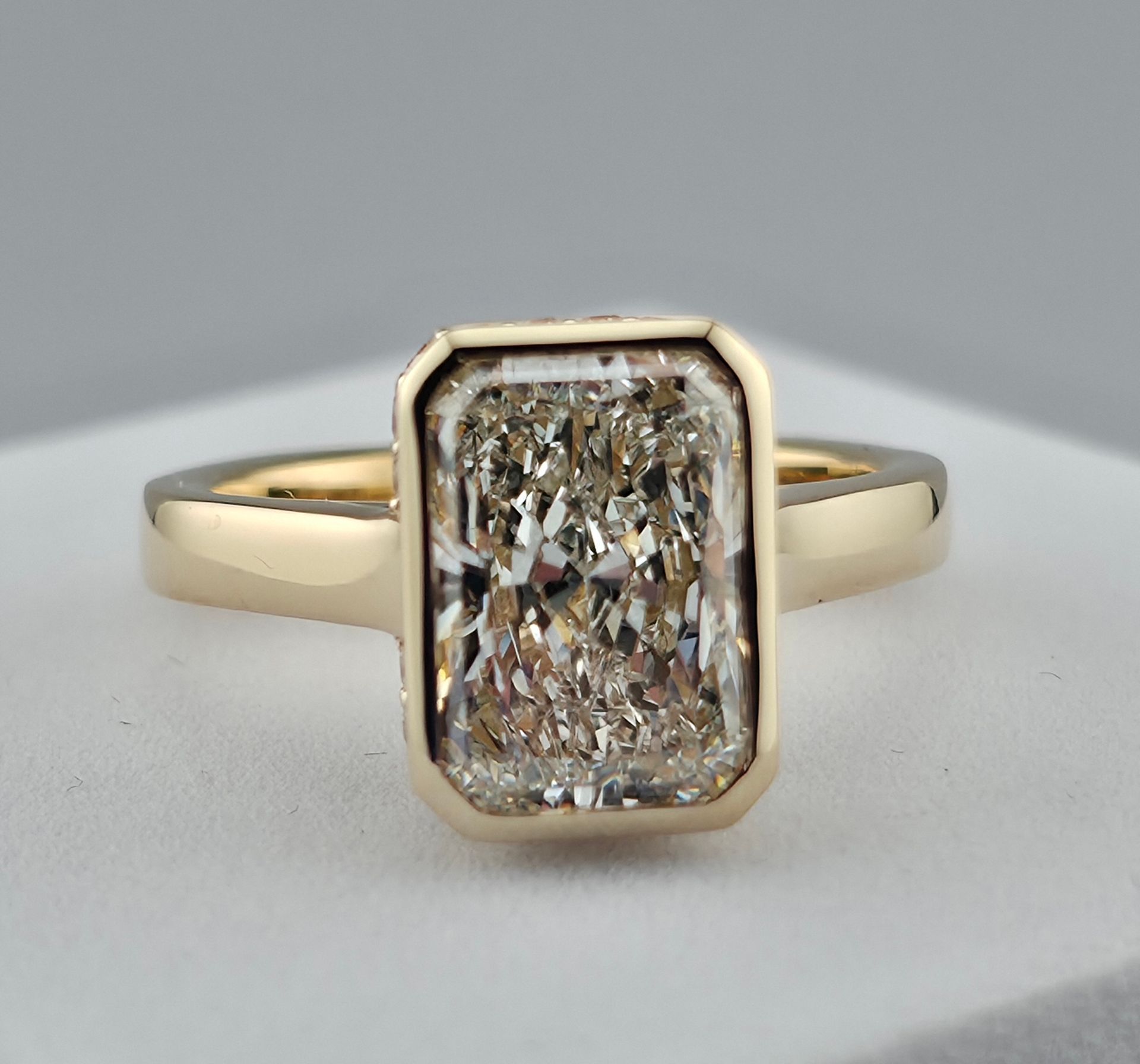 Gold ring with a rectangular radiant Cut diamond on a light gray background