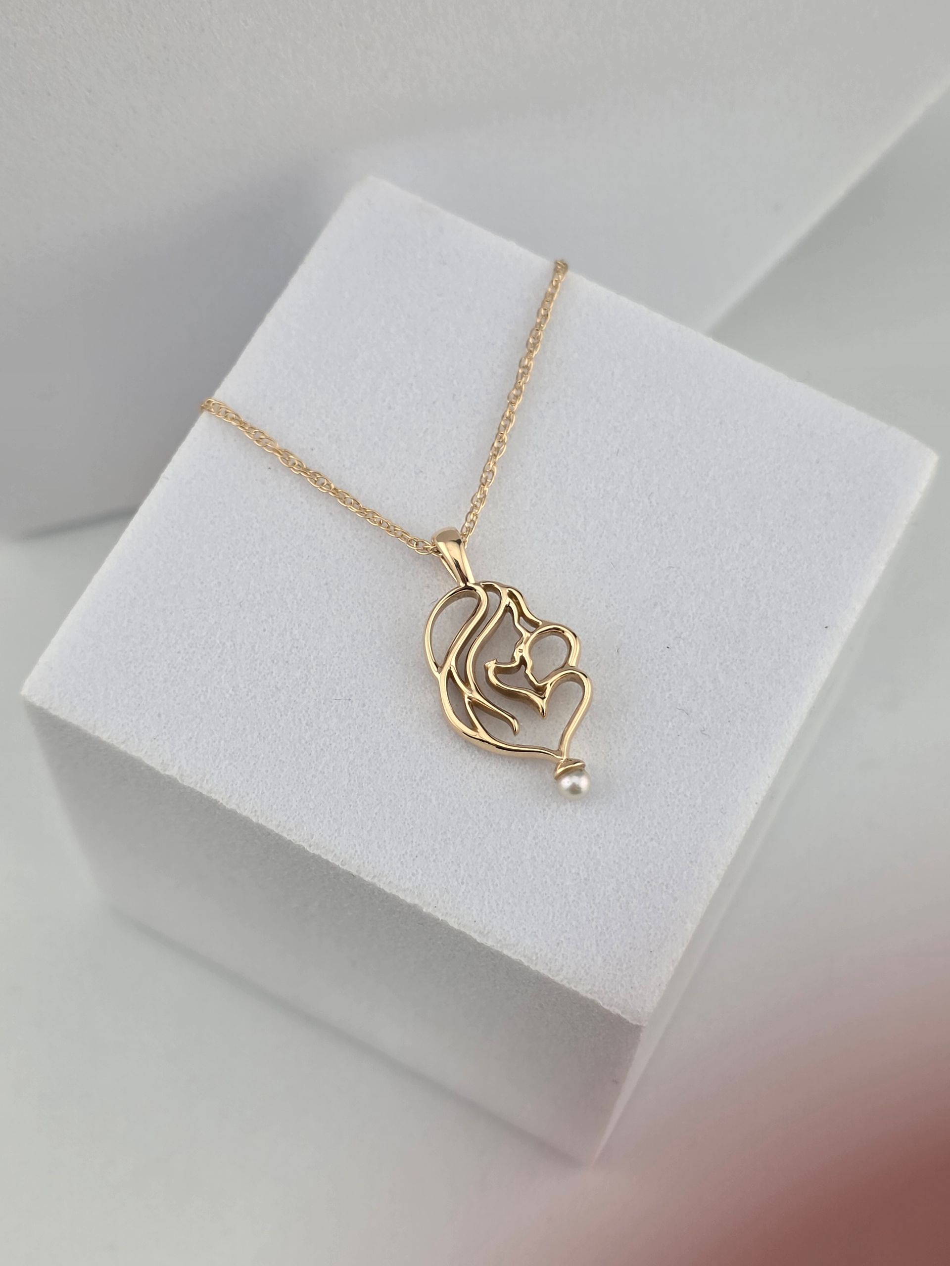 Gold necklace with a heart pendant on a white display stand