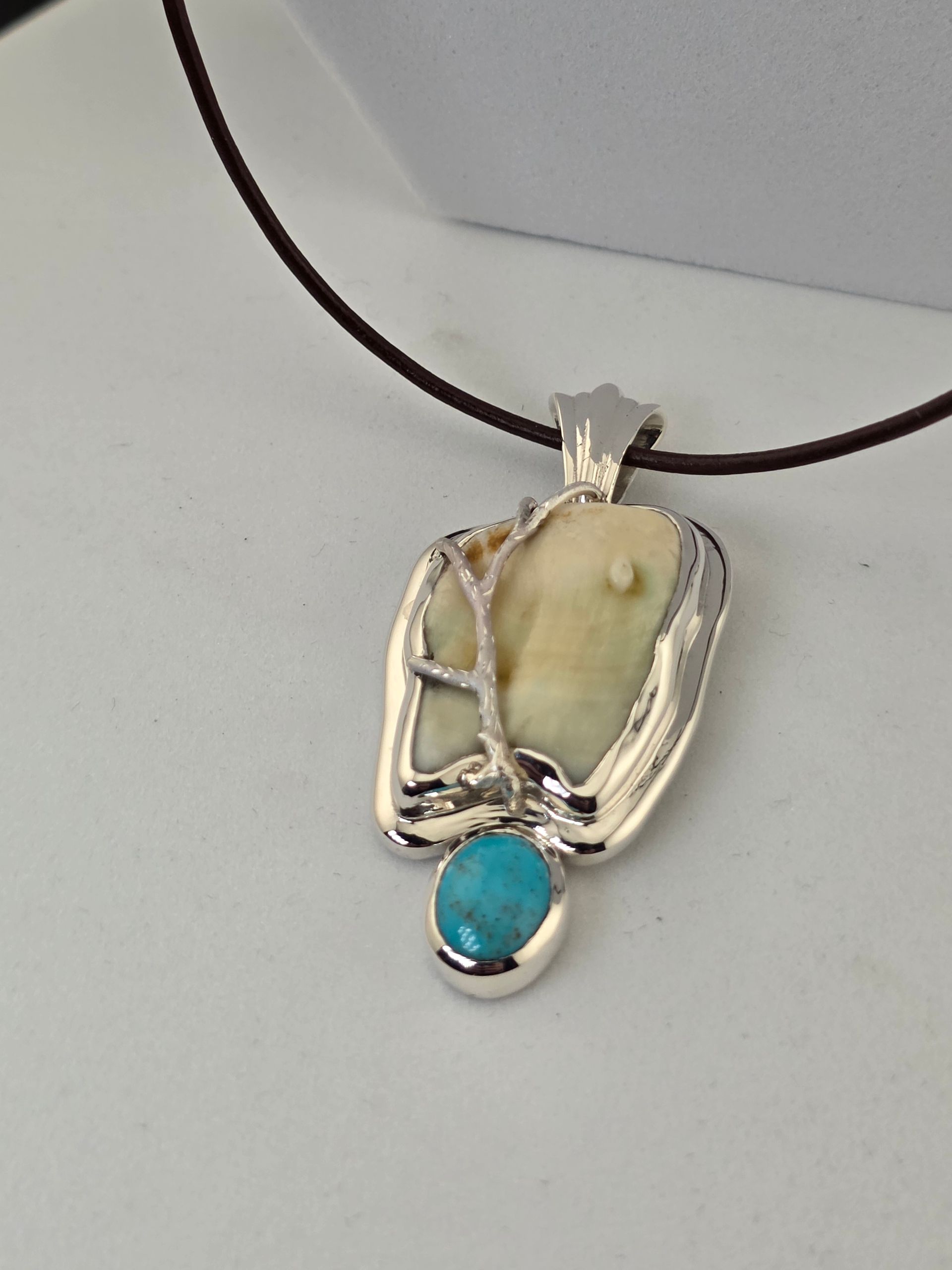 Silver wire-wrapped pendant with a elk ivory stone and turquoise-blue gem on a black cord necklace