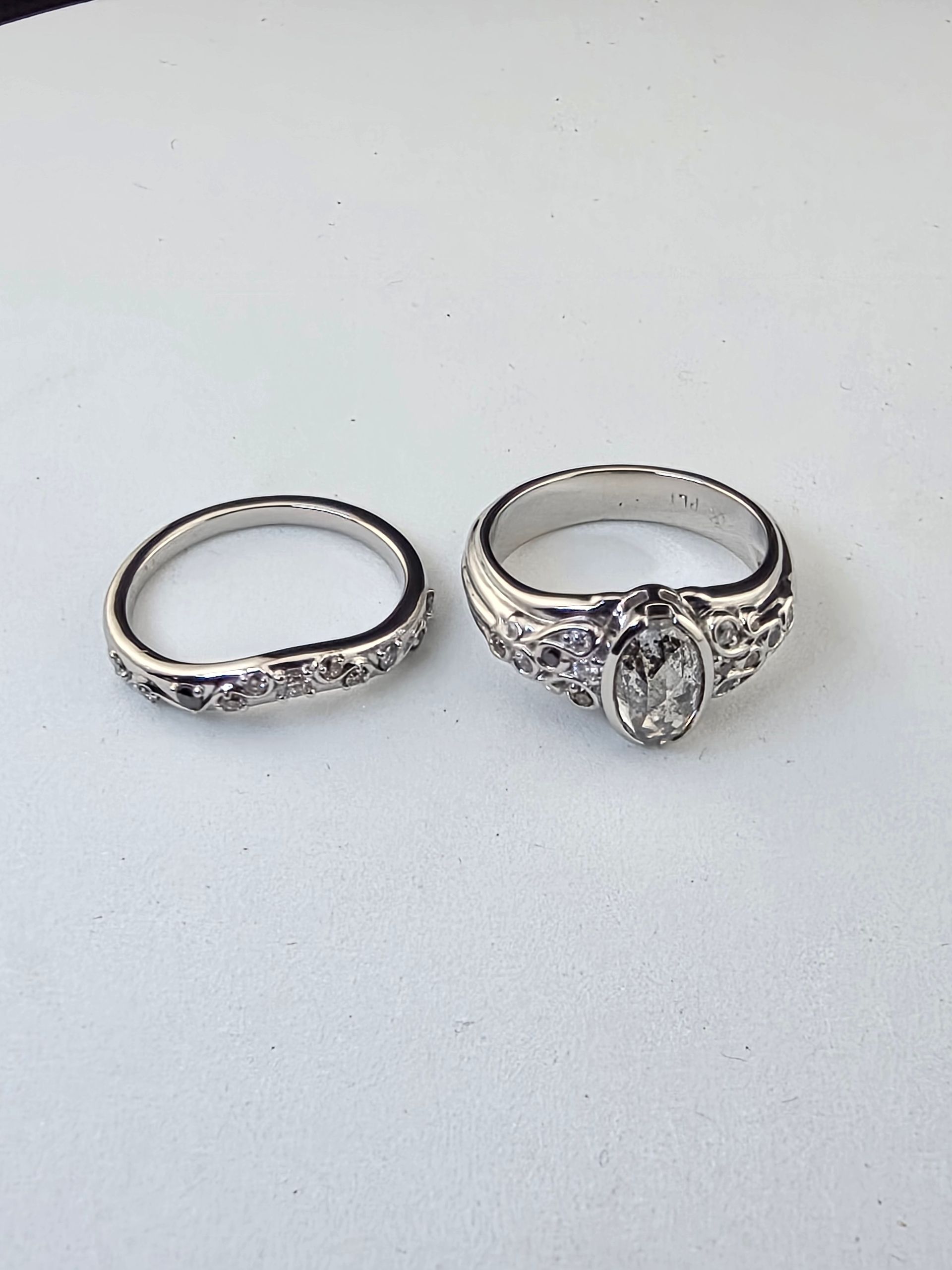 White wedding set rings with multi color salt/pepper diamonds on a white background, one with a central gemstone and one plain