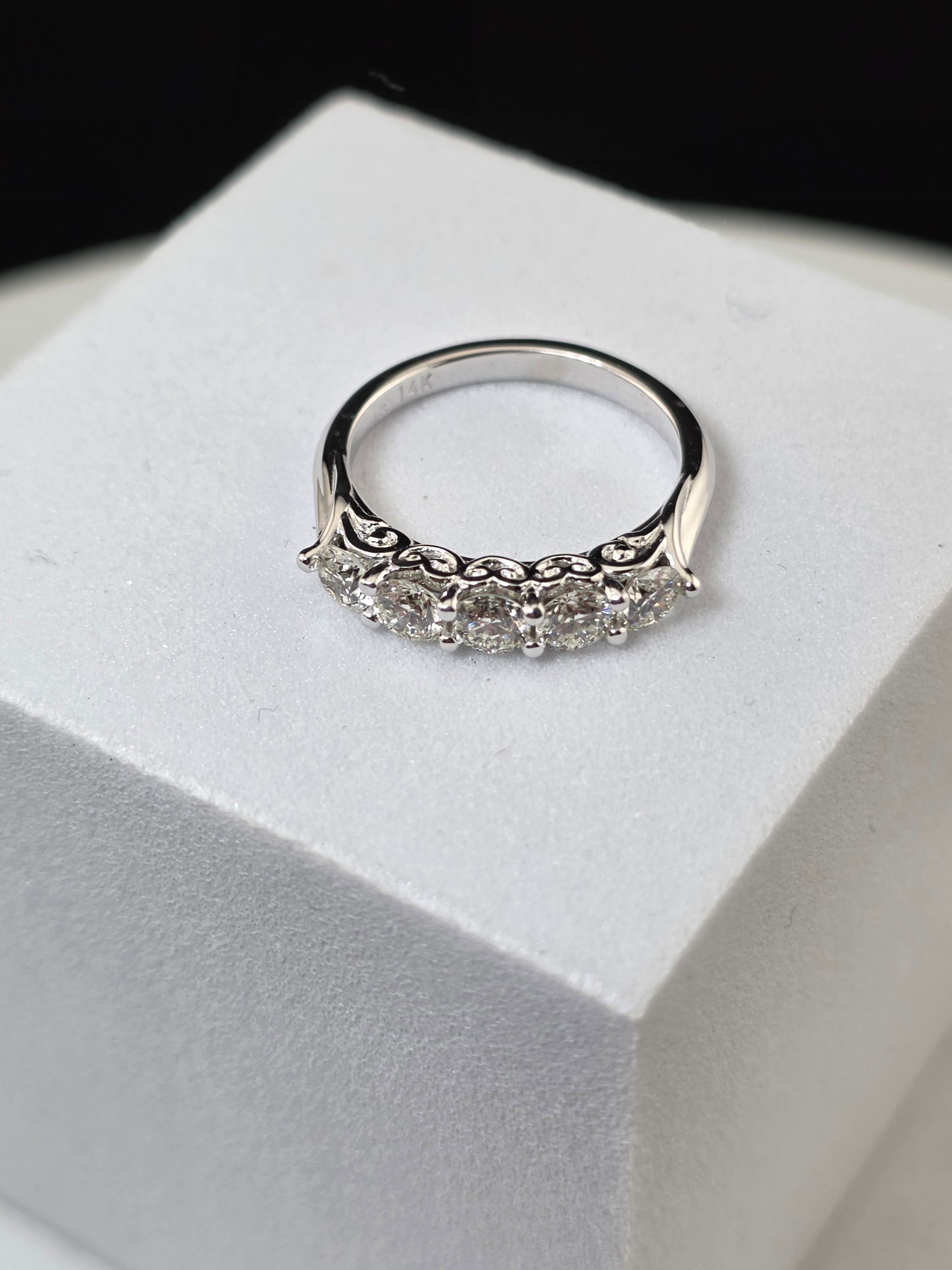 Silver ring with a row of small diamonds on a white display stand